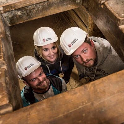 Drei Besucher schauen durch eine Luke im Bergwerk Escape-Room
