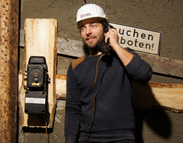 Werde Gamemaster (m/w/d) im EscapeRoom Junger Mann mit Schutzhelm telefoniert mit einem alten Bergwerkstelefon