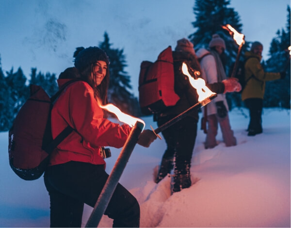 Eine Gruppe junger Menschen wandern mit Fackeln durch tiefen Schnee 